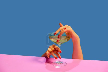 Téléchargez les photos : Mains féminines tenant un verre de champagne sur fond rose bleu. Fête. Concept de vacances, fête, boisson. Couleurs complémentaires. Espace de copie pour l'annonce. Pop art. Espace de copie pour la publicité - en image libre de droit