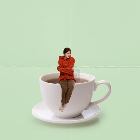 Téléchargez les photos : Contemporary art collage. Creative design. Young girl feeling cold, sitting on cup with warm hot tea over mint background. Concept of hot drinks, coziness, taste, emotions, lifestyle. Poster, ad - en image libre de droit