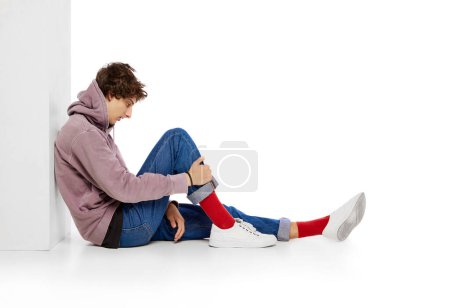 Foto de Young boy in casual clothes sitting with thoughtful face over white background. feeling depression and emotional breakdown. Concept of psychology, inner world, mental health, emotions, feelings - Imagen libre de derechos