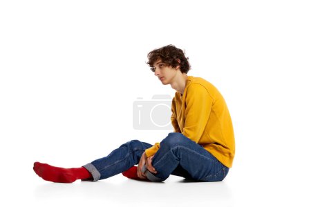 Photo for Portrait of young boy sitting on floor in sadness, feeling asocial over white background. Loneliness, depression. Concept of psychology, inner world, mental health, emotions, feelings - Royalty Free Image