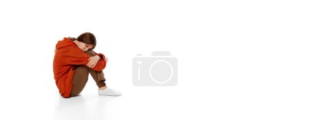 Téléchargez les photos : Teen girl sitting on floor over white background. Feeling stressful, sad, depressed and lonely. Youth anxiety problems. Concept of psychology, inner world, mental health. Copy space for ad, banner - en image libre de droit