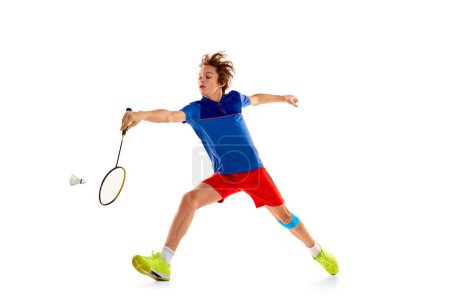 Téléchargez les photos : Portrait of teen boy in uniform playing badminton, gitting shuttlecock in a run isolated over white background. Concentration. Concept of sportive lifestyle, motion, action, competition, hobby - en image libre de droit