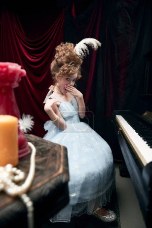 Photo for Portrait of cute little girl, child in image of medieval royal person in fabulous dress sitting at the piano. Concept of historical remake, comparison of eras, medieval fashion, emotions, childhood - Royalty Free Image