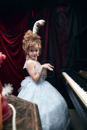 Téléchargez les photos : Adorable little girl, child in image of medieval royal person in cute dress sitting at the piano and emotionally posing. Concept of historical remake, comparison of eras, medieval fashion, childhood - en image libre de droit