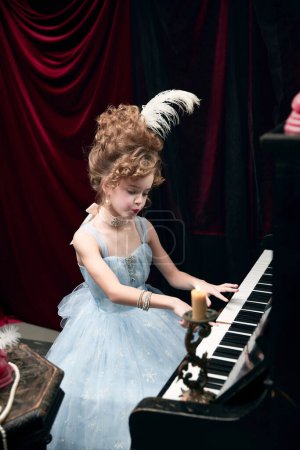 Téléchargez les photos : Portrait of beautiful little girl, child in image of medieval royal person in elegant dress sitting at the piano, playing. Concept of historical remake, comparison of eras, medieval fashion, childhood - en image libre de droit