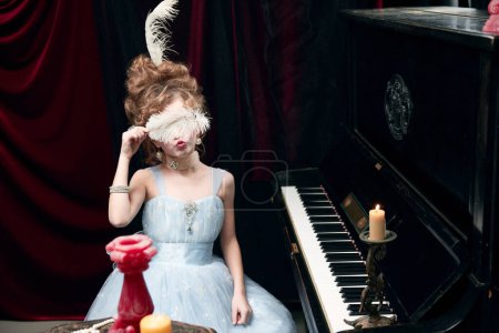 Téléchargez les photos : Little girl, child in image of medieval person in beautiful dress sitting at the piano and covering eyes with feather. Concept of historical remake, comparison of eras, medieval fashion, childhood - en image libre de droit