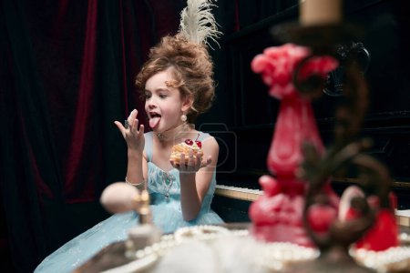 Portrait of cute little girl, child in image of medieval royal person funny eating cake. Enjoyment. Concept of historical remake, comparison of eras, medieval fashion, emotions, childhood