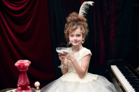 Photo for Portrait of cute little girl, child in image of medieval royal person sitting at the piano with milkshake. Concept of historical remake, comparison of eras, medieval fashion, emotions, childhood - Royalty Free Image