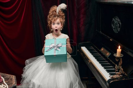 Photo for Portrait of cute little girl, child in image of medieval royal person emotionally opening presents. Surprise. Concept of historical remake, comparison of eras, medieval fashion, emotions, childhood - Royalty Free Image