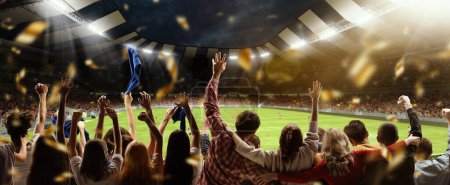 Téléchargez les photos : Back view of football, soccer fans cheering their team, holding flag at crowded stadium at evening time. Concept of sport, cup, world, team, event, competition, hobby, lifestyle, emotions - en image libre de droit