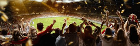 Foto de Back view of football, soccer fans cheering their team with flag and posotove emotions at crowded stadium at evening time. Concept of sport, cup, world, team, event, competition - Imagen libre de derechos