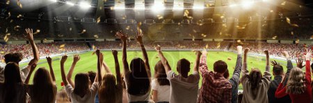 Téléchargez les photos : Back view of football, soccer fans emotionally cheering their team at crowded stadium at evening time. Hobby of millions of people. Concept of sport, cup, world, team, event, competition - en image libre de droit