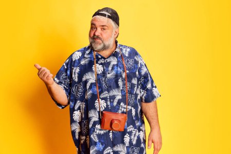 Téléchargez les photos : Portrait of fat mature man in stylish shirt posing over bright yellow studio background. Travelling as hobby. Concept of american style, culture, emotions, facial expression, lifestyle - en image libre de droit