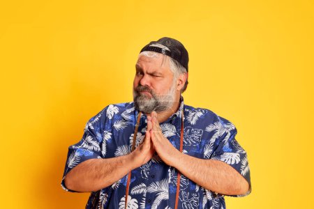 Photo for Portrait of fat mature man in stylish shirt posing with funny grimace face over bright yellow studio background. Concept of american style, culture, emotions, facial expression, lifestyle - Royalty Free Image