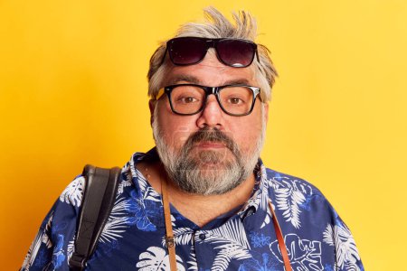 Photo for Portrait of fat mature man in stylish shirt posing with glasses and sunglasses over bright yellow studio background. Concept of american style, culture, emotions, facial expression, travel - Royalty Free Image