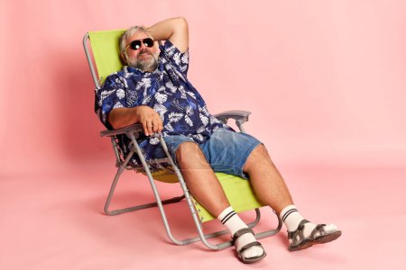 Foto de Portrait of mature man in stylish shirt and sunglasses lying, posing over pink studio background. Relaxation, vacation. Concept of american style, culture, emotions, facial expression, lifestyle - Imagen libre de derechos