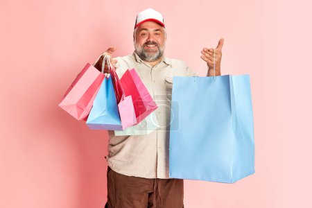 Téléchargez les photos : Portrait of mature man in casual clothes going shopping, posing with shopping trolley over pink studio background. Good sales. Concept of american style, culture, emotions, facial expression - en image libre de droit