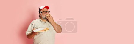 Foto de Portrait of mature man in casual clothes eating delicious Italian pizza over pink studio background. Banner, flyer. Concept of american style, culture, emotions, facial expression, lifestyle - Imagen libre de derechos