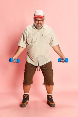 Photo for Portrait of mature overweight man training with dumbbells over pink studio background. Motivation to lose weight. Concept of american style, culture, emotions, facial expression, lifestyle, sport - Royalty Free Image