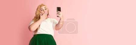 Photo for Portrait of stylish woman posing, taking selfie with phone or having online video call over pink studio background. Banner. Concept of american style, culture, emotions, facial expression, lifestyle - Royalty Free Image