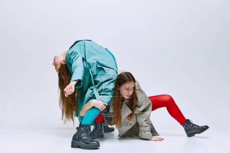 Téléchargez les photos : Portrait of two young women in bright red and blue tights and coat posing over grey studio background. Feedom. Concept of modern fashion, queer, art photography, weird people, creativity - en image libre de droit