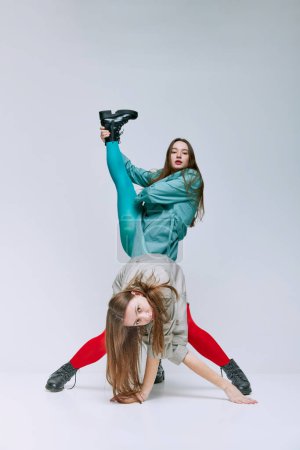 Foto de Portrait of two young women in bright red and blue tights and coat posing over grey studio background. Weirdness. Concept of modern fashion, queer, art photography, weird people, creativity - Imagen libre de derechos
