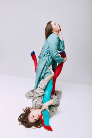 Téléchargez les photos : Portrait of two young girls in bright red and blue tights and coat posing over grey studio background. Self-expression. Concept of modern fashion, queer, art photography, weird people, creativity - en image libre de droit