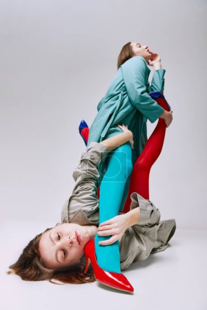 Foto de Extraordinary behaviour. Portrait of two young girls in bright red, blue tights and coat posing over grey studio background. Concept of modern fashion, queer, art photography, weird people, creativity - Imagen libre de derechos
