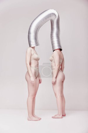 Téléchargez les photos : Futuristic communication. Creative photography with two young girls posing in nude underwear over beige studio background. Concept of cringe, queer, art photography, weird people, creativity - en image libre de droit