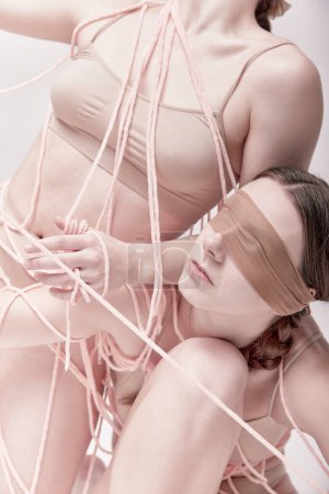 Cropped portrait of two young girls posing in underwear and ropes with eyes closed over light studio background. Concept of modern fashion, queer, art photography, weird people, creativity