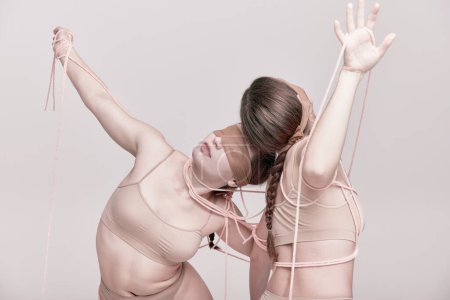 Foto de Connection. Portrait of two young girls posing in underwear and ropes with eyes closed over light studio background. Concept of modern fashion, queer, art photography, weird people, creativity - Imagen libre de derechos