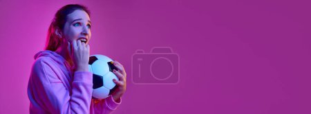 Téléchargez les photos : Tense feelings. Portrait of young emotive girl posing with football ball background in neon light. Banner, flyer. Concept of youth, beauty, fashion, lifestyle, emotions, facial expression. Ad - en image libre de droit