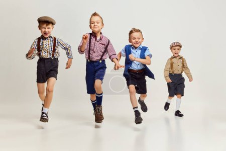 Téléchargez les photos : Active, playful boys, children in stylish clothes with suspenders playing together, running over grey background. Concept of game, childhood, friendship, activity, leisure time, retro style, fashion. - en image libre de droit