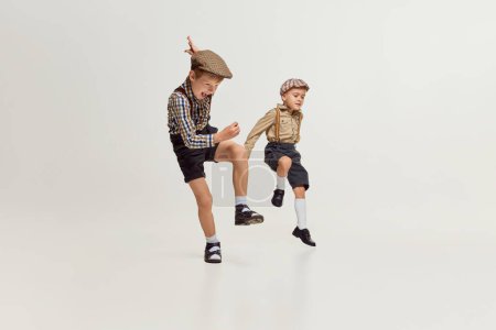 Téléchargez les photos : Active boys, children in stylish classical clothes playing together, running, jumping over grey background. Fun. Concept of game, childhood, friendship, activity, leisure time, retro style, fashion. - en image libre de droit