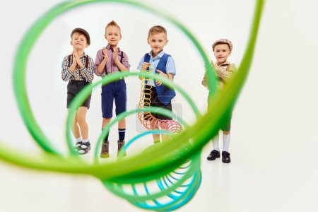 Téléchargez les photos : Boys, children in classical retro clothes playing with slinky toy over grey studio background. Competition. Concept of game, childhood, friendship, activity, leisure time, retro style, fashion. - en image libre de droit