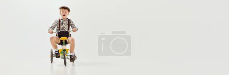 Photo for Boy, child in retro clothes riding vintage bicycle over grey studio background. Banner, flyer. Concept of game, childhood, friendship, activity, leisure time, retro style, fashion. - Royalty Free Image