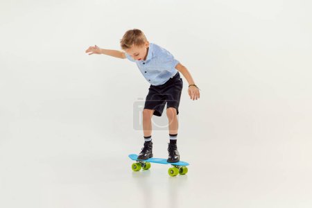Téléchargez les photos : Balancing. Playful, active kid, boy riding on skateboard over grey studio background. Concept of game, childhood, friendship, activity, leisure time, retro style, fashion. - en image libre de droit