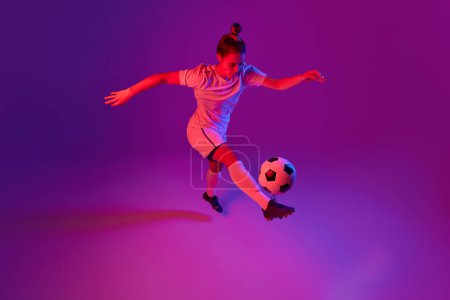 Photo for Dribbling. Young professional female football, soccer player in motion, training, playing over gradient pink background in neon light. Concept of sport, action, motion, goals, competition, hobby, ad. - Royalty Free Image