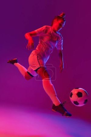 Téléchargez les photos : Young professional female football, soccer player in motion, training, playing over gradient pink background in neon light. Concept of sport, action, motion, goals, competition, hobby, ad. - en image libre de droit