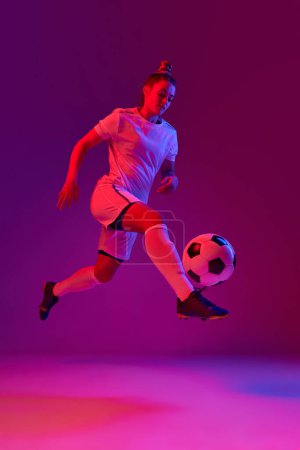 Foto de Concentration. Young professional female football, soccer player in motion, training, playing over gradient pink background in neon. Concept of sport, action, motion, goals, competition, hobby, ad. - Imagen libre de derechos