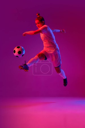 Téléchargez les photos : Young professional female football, soccer player in motion, training, playing over gradient pink background in neon light. Jump kick. Concept of sport, action, motion, goals, competition, hobby, ad. - en image libre de droit