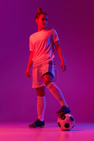 Photo for Young girl, professional female football, soccer player posing with ball over gradient pink background in neon light. Concept of sport, action, motion, goals, competition, hobby, ad. - Royalty Free Image