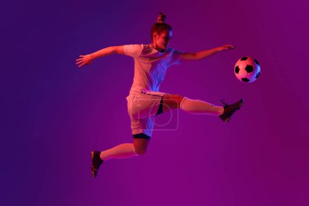 Foto de Young professional female football, soccer player in motion, training, playing over gradient pink background in neon light. Hitting in a jump. Concept of sport, action, goals, competition, hobby, ad. - Imagen libre de derechos
