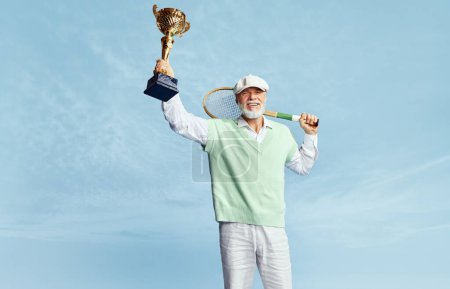 Foto de Trophy, winner. Portrait of handsome senior man in stylish outfit posing with tennis racket over sky blue background. Concept of leisure activity, hobby, lifestyle, fitness, emotions, retro style - Imagen libre de derechos