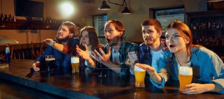 Photo for Group of young people, men and women watching match at pub. Fans emotionally cheering up favourite sport team. Tense moment of game. Competition, championship, match translation. Emotions. - Royalty Free Image