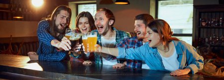 Foto de Happy young people, friends meeting at pub to watch sport match. Fans emotionally cheering up favourite sport team. Drinking beer. Win. Competition, championship, match translation. Emotions. - Imagen libre de derechos