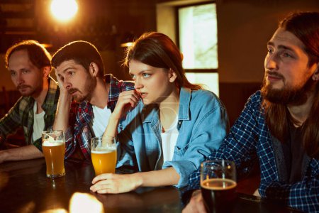 Photo for Group of young people, fans, men and women watching match at pub. Tense game moment. Losing goal. Competition, championship, match translation. Emotions. Drinking beer - Royalty Free Image
