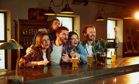 Foto de Friends, young people, men and women watching match at pub. Fans emotionally cheering up favourite sport team. Winning game of favorite team. Competition, championship, match translation. Emotions. - Imagen libre de derechos
