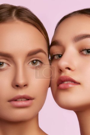 Foto de Close-up portrait of two young, beautiful girls with well-kept skin isolated over pink studio background. Nude makeup. Concept of skincare, cosmetology, natural beauty, youth, spa, cosmetics. Ad - Imagen libre de derechos