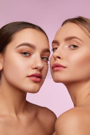 Foto de Portrait of two young, beautiful girls with well-kept skin isolated over pink studio background. Nude, natural makeup. Concept of skincare, cosmetology, natural beauty, youth, spa, cosmetics. Ad - Imagen libre de derechos